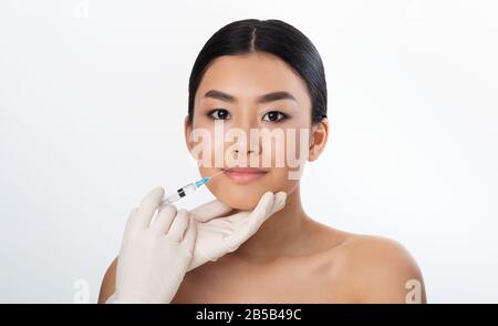 Korean Girl Receiving Injection During Lips Plumping Procedure, White Background Stock Photo