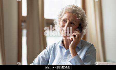 Smiling senior woman having cellphone talk at home Stock Photo