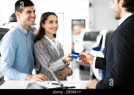 Couple Buying Car Giving Seller Credit Card In Dealership Office Stock Photo