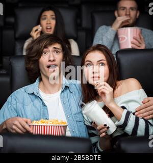 Leisure activity. Emotional young man with his girlfriend watching thriller in movie theater Stock Photo