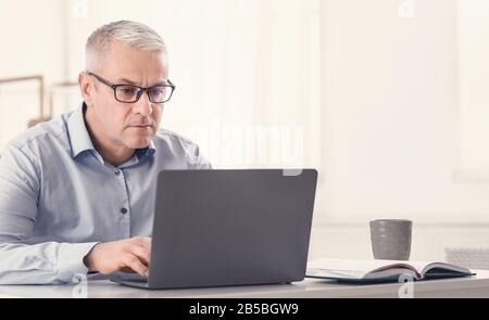 Serious senior man using laptop at home Stock Photo