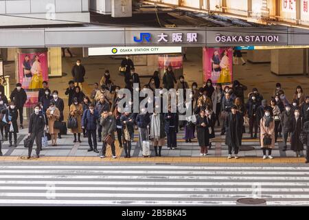 Osaka, Japan - March 4, 2020: Crowd of people wearing masks wait to cross street in front of JR Osaka Station Stock Photo