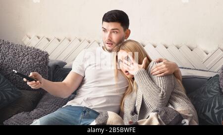 Terrified young couple watching scary movie at home Stock Photo