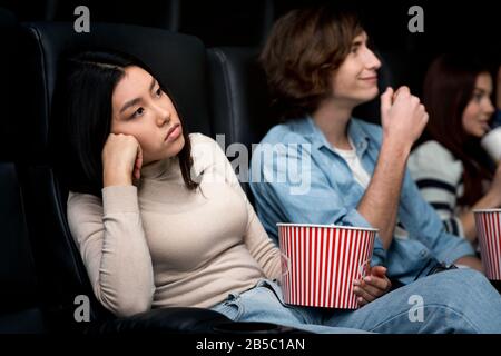 Dull date. Bored young lady with boyfriend watching movie in cinema Stock Photo