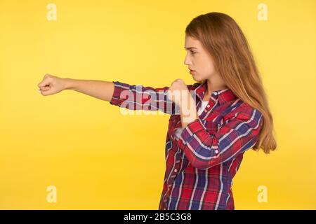 Profile of strong and determined ginger girl in checkered shirt punching air with fist and looking self-confident, female struggle, fighting spirit. i Stock Photo