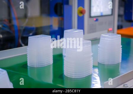 Stack of food containers on conveyor belt of plastic injection molding machine Stock Photo