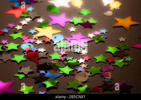 Confetti scattered on a black table background. Stars and other colourful shapes made from multicoloured foil. Stock Photo