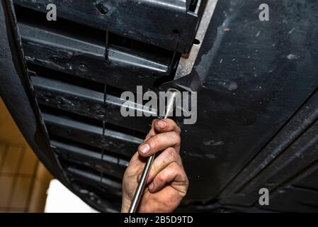 The car mechanic unscrews the bottom plastic engine cover using a socket wrench. Stock Photo