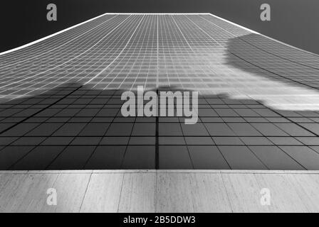 Abstract image of vertical view of glass window skyscraper against deep blue sky, in black and white. Stock Photo