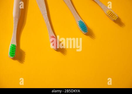 Four eco bamboo kid colorful toothbrushes on the yellow background. Stock Photo