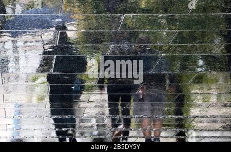 Blurry abstract reflection silhouette of three people walking under umbrella on a wet city street puddle on pedestrian promenade on a rainy day Stock Photo