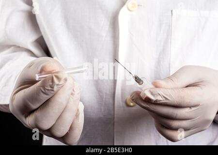 doctor in a white coat and gloves holds opens a syringe close-up. vaccination an injection treatment cold flu measles covid-19.