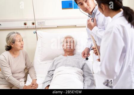 young asian doctor examining elderly patient discussing his medical condition in hospital ward Stock Photo