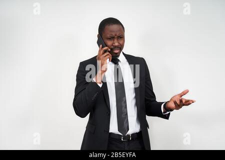Closeup of angry young african man screaming while talking on smartphone over grey background Stock Photo