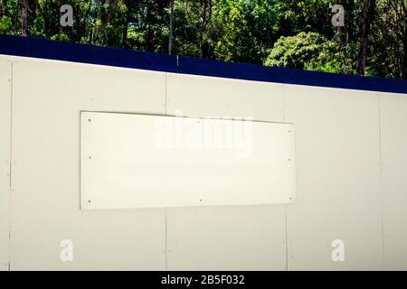 A rectangular white advertising signboard attached on the blue-white background with foresty area behind it Stock Photo