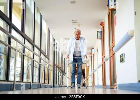 senior asian man walking using a walker in hallway of nursing home Stock Photo