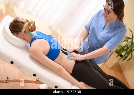 Physical therapist applying kinesio tape on female patient's lower back. Kinesiology, physical therapy, rehabilitation concept. Stock Photo