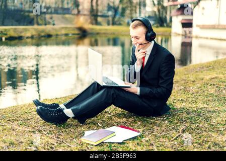 businessman in headphones talking on the laptop. Internet communication. young guy in a suit on the nature. freelancer, distant work Stock Photo