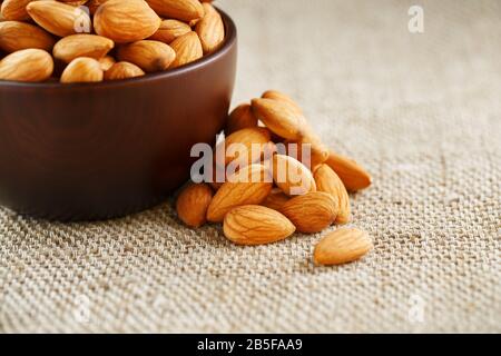 Almonds in a wooden cup on a burlap cloth background. Golden almond closeup in dark brown cup Stock Photo