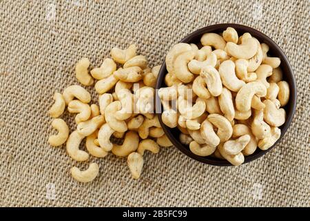 Cashew nuts in a wooden bowl on a burlap cloth background. Golden cashew close-up in a dark brown cup. Stock Photo