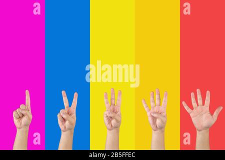 Asian hand counts 1 to 5 by finger on the seperated - saturated rainbow such as pink blue yellow orange and red sections background. Stock Photo