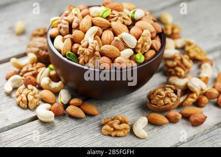 Wooden bowl with mixed nuts on a wooden gray background. Healthy food and snacks, organic vegetarian meals. Walnut, pistachios, almonds, hazelnuts and Stock Photo
