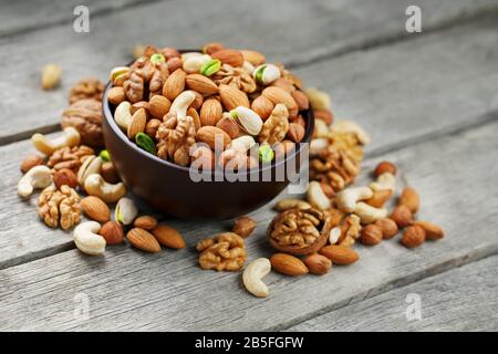 Wooden bowl with mixed nuts on a wooden gray background. Healthy food and snacks, organic vegetarian meals. Walnut, pistachios, almonds, hazelnuts and Stock Photo