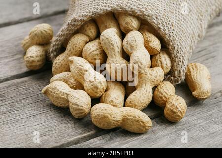 Peanuts in a miniature burlap bag on old, gray wooden surface. Unclean peanuts on wooden table. Macro Stock Photo