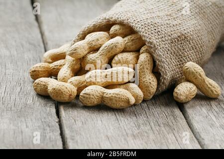 Peanuts in a miniature burlap bag on old, gray wooden surface. Unclean peanuts on wooden table. Macro Stock Photo