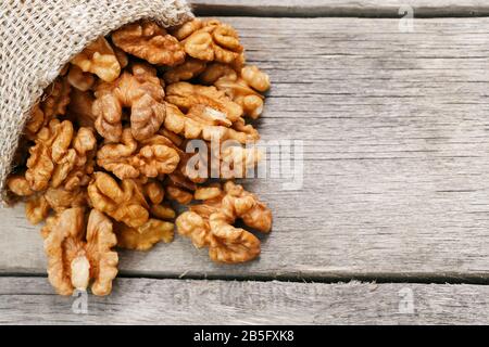 Walnuts in a burlap bag on a wooden background. Walnut macro - edible kernels of seeds. Healthy and healthy food for vegetarians Stock Photo