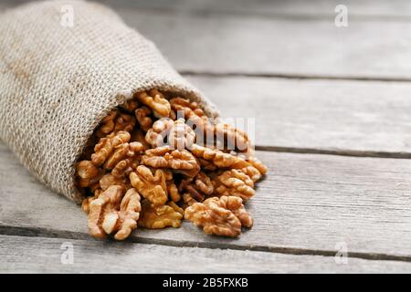 Walnuts in a burlap bag on a wooden background. Walnut macro - edible kernels of seeds. Healthy and healthy food for vegetarians Stock Photo