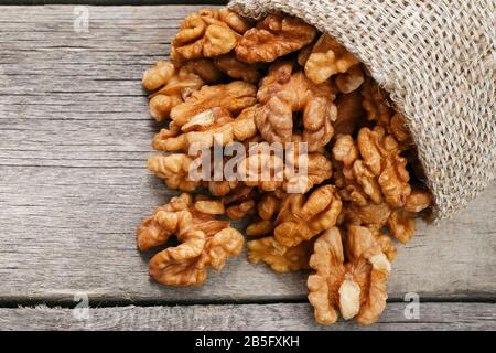 Walnuts in a burlap bag on a wooden background. Walnut macro - edible kernels of seeds. Healthy and healthy food for vegetarians Stock Photo