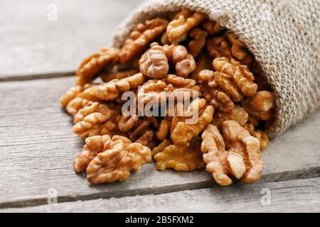 Walnuts in a burlap bag on a wooden background. Walnut macro - edible kernels of seeds. Healthy and healthy food for vegetarians Stock Photo