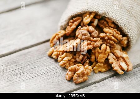 Walnuts in a burlap bag on a wooden background. Walnut macro - edible kernels of seeds. Healthy and healthy food for vegetarians Stock Photo