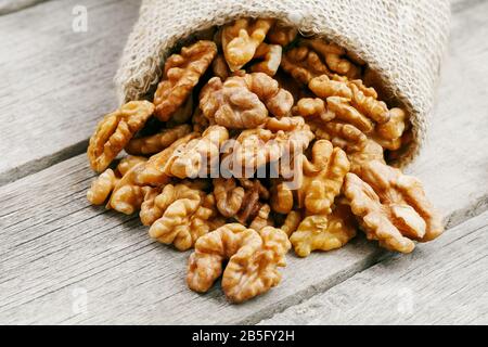 Walnuts in a burlap bag on a wooden background. Walnut macro - edible kernels of seeds. Healthy and healthy food for vegetarians Stock Photo