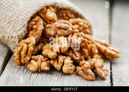 Walnuts in a burlap bag on a wooden background. Walnut macro - edible kernels of seeds. Healthy and healthy food for vegetarians Stock Photo
