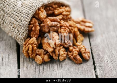 Walnuts in a burlap bag on a wooden background. Walnut macro - edible kernels of seeds. Healthy and healthy food for vegetarians Stock Photo