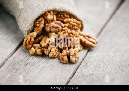 Walnuts in a burlap bag on a wooden background. Walnut macro - edible kernels of seeds. Healthy and healthy food for vegetarians Stock Photo