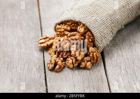 Walnuts in a burlap bag on a wooden background. Walnut macro - edible kernels of seeds. Healthy and healthy food for vegetarians Stock Photo
