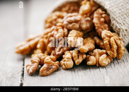 Walnuts in a burlap bag on a wooden background. Walnut macro - edible kernels of seeds. Healthy and healthy food for vegetarians Stock Photo