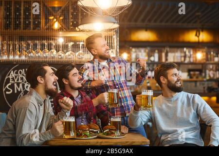 A group of young bearded guys watching sports on tv in a pub bar. Stock Photo