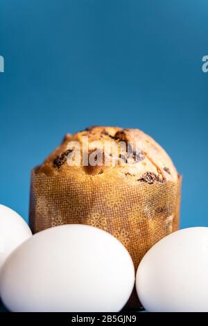 Easter composition from a small Easter cake and three white chicken eggs on a classic blue background close-up. Close-up of Easter cake and eggs on a Stock Photo