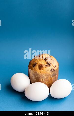 Easter composition from a small Easter cake and three white chicken eggs on a classic blue background close-up. Close-up of Easter cake and eggs on a Stock Photo