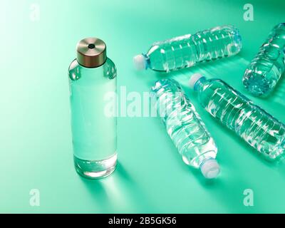 Zero waste concept - reusable glass water bottle vs single use plastic bottle on mint green background Stock Photo