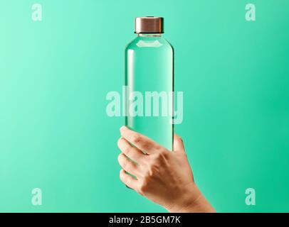 Hand holding reusable glass water bottle with stainless steel cap on mint green background Stock Photo