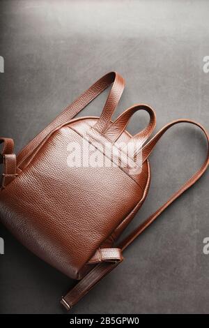 Brown backpack made of textured brown leather on a black stone background. Elegant golden brown women backpack with fashion and rivets. Genuine leathe Stock Photo