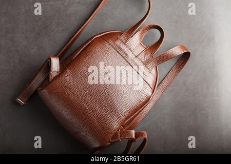Brown backpack made of textured brown leather on a black stone background. Elegant golden brown women backpack with fashion and rivets. Genuine leathe Stock Photo