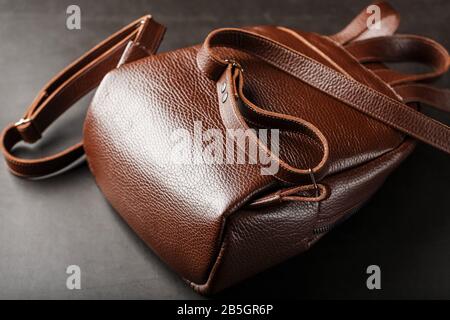 Brown backpack made of textured brown leather on a black stone background. Elegant golden brown women backpack with fashion and rivets. Genuine leathe Stock Photo