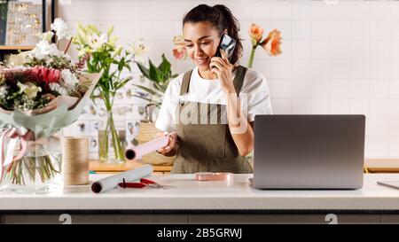 Female florist standing in flower shop. Young woman talking on mobile phone. Stock Photo
