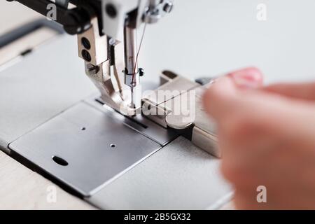 A leather craftsman produces leather goods on a sewing machine in his shop. Handmade work. Close up. Stock Photo